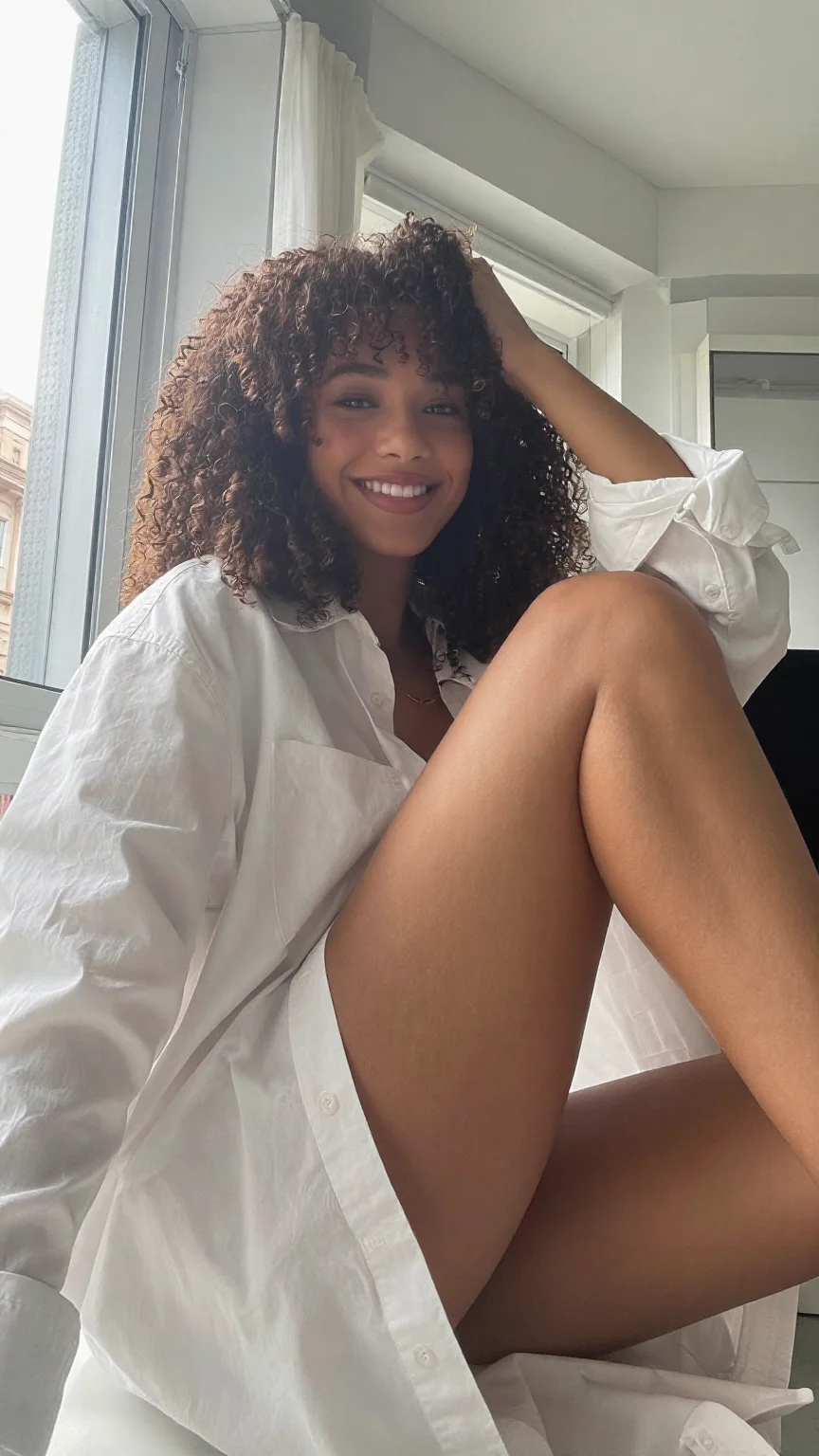 Mixed-race woman with curly hair in oversized white shirt in window